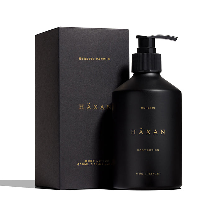 A matte black pump bottle of HÄXAN body lotion by Heretic Parfum, standing next to its matching matte black box on a clean white background.